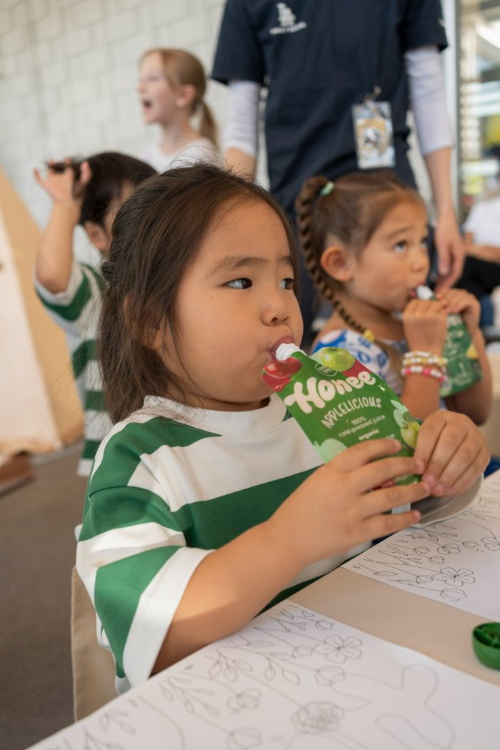 A young girl sipping a Honee Applelicious pouch