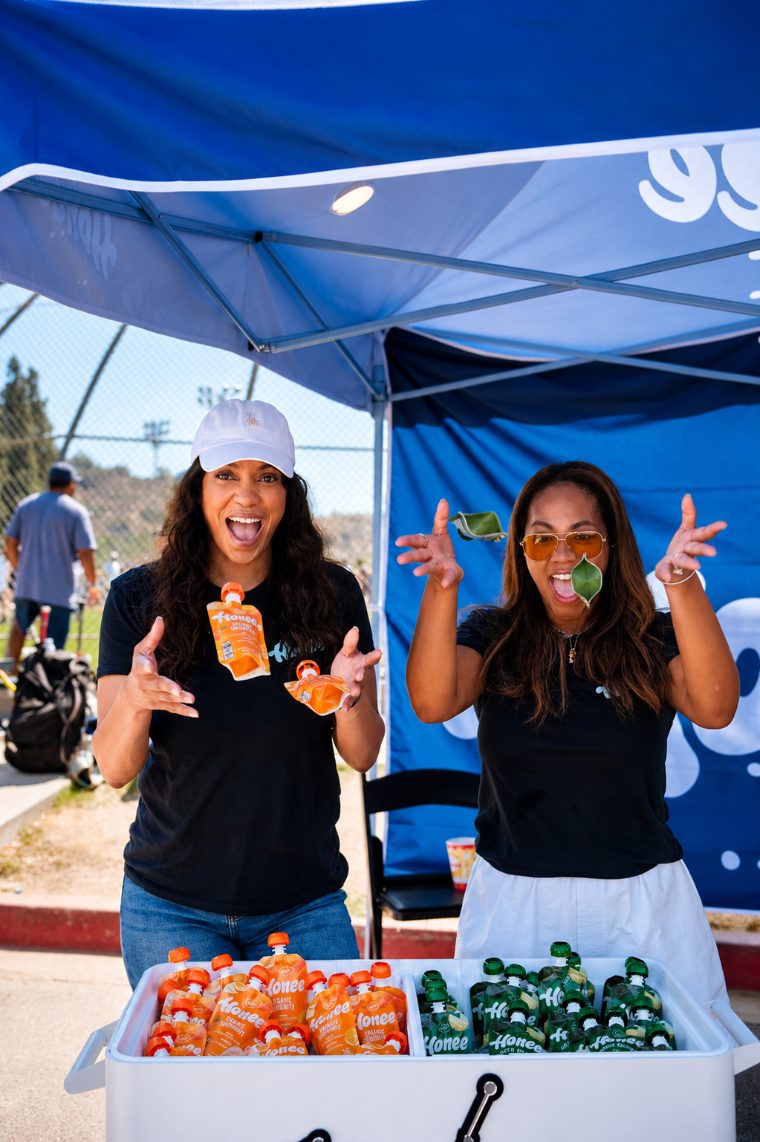 Two team members having fun with Honee pouches behind the cooler