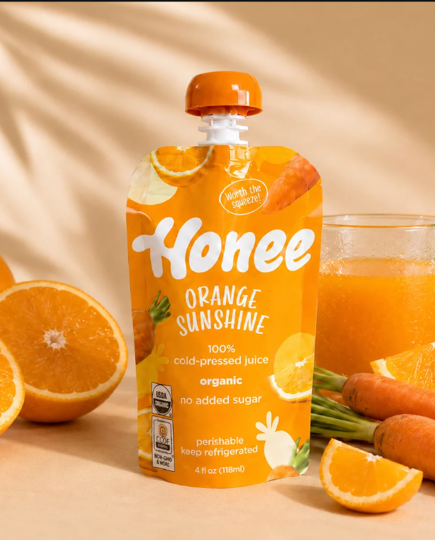 Honee Orange Sunshine pouch with fresh fruit and a glass of juice